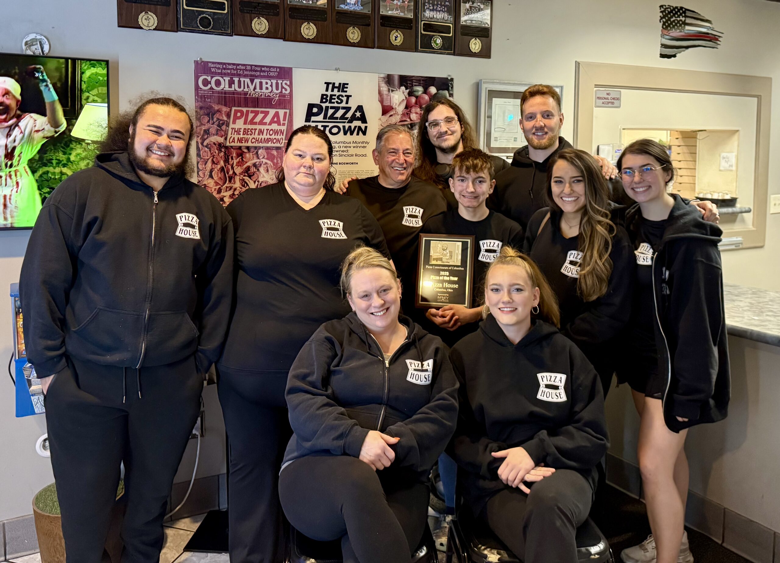 Pizza House staff pose together, proudly holding an award for their achievements. The image highlights camaraderie and showcases their recognition in a vibrant setting.