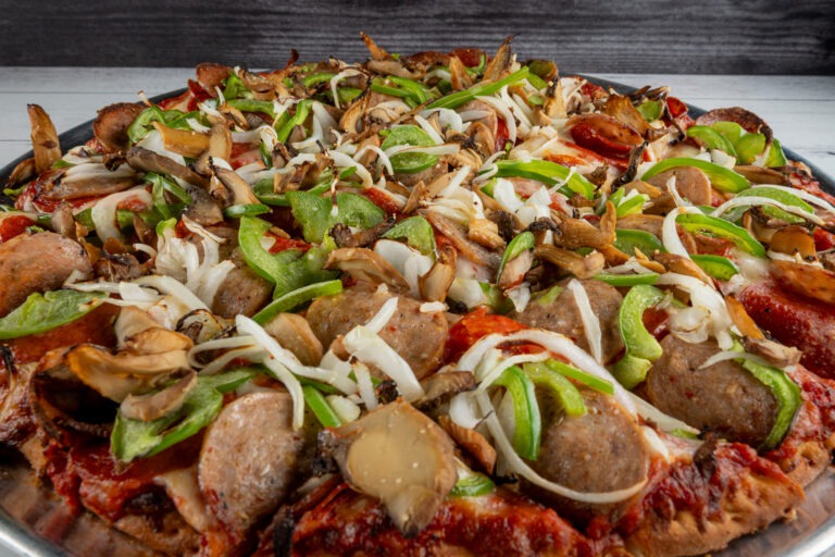 A large, circular pizza topped with pepperoni, green peppers, onions, and mushrooms, served on a metal tray against a white wooden background.